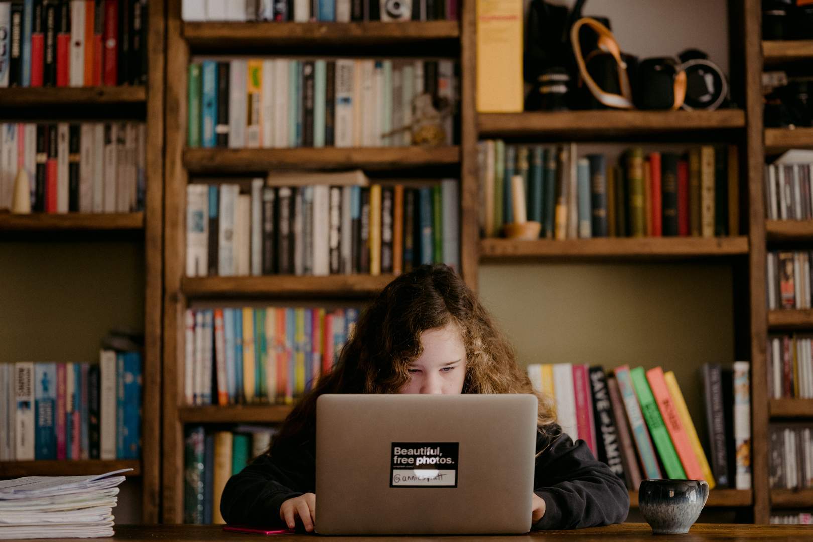 Meisje achter laptop voor boekenkast