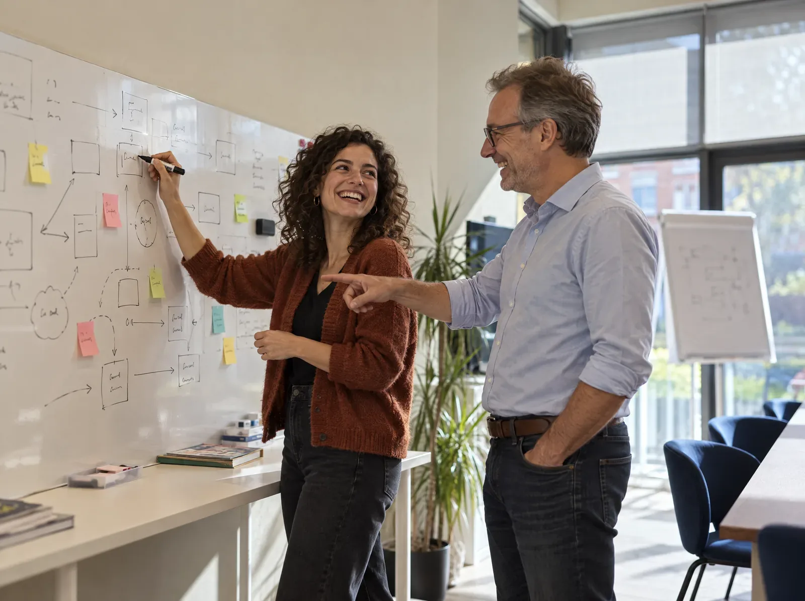 Twee collega's lachen bij een whiteboard met een schets van een systeem