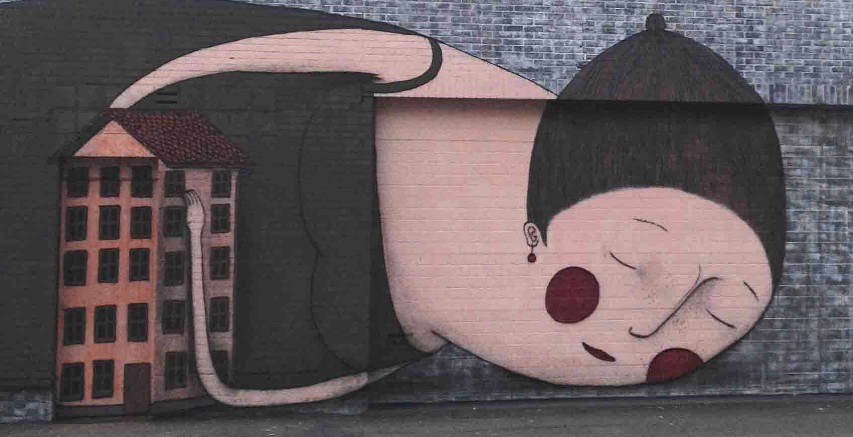 Muurschildering van een slapende vrouw met haar armen rond een flatgebouw