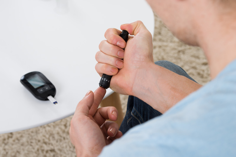 Iemand neemt een vingerprik met een prikpen. De glucosemeter ligt op tafel.
